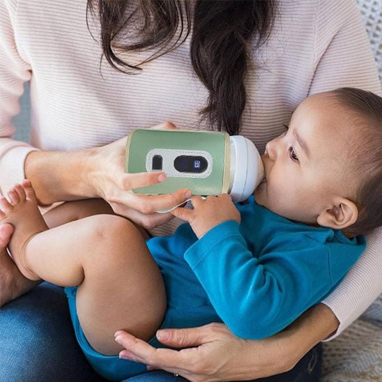 Bébé buvant son lait grâce à un chauffe biberon nomade dans les bras de sa maman
