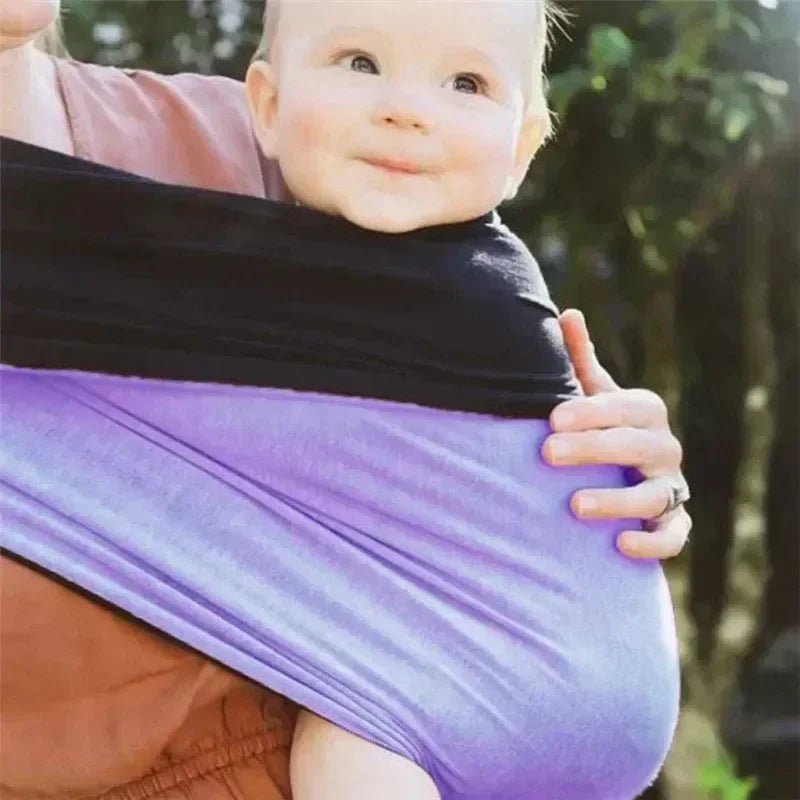 Bébé heureux et amusant porté en écharpe noire et mauve, confort et proximité maman-bébé