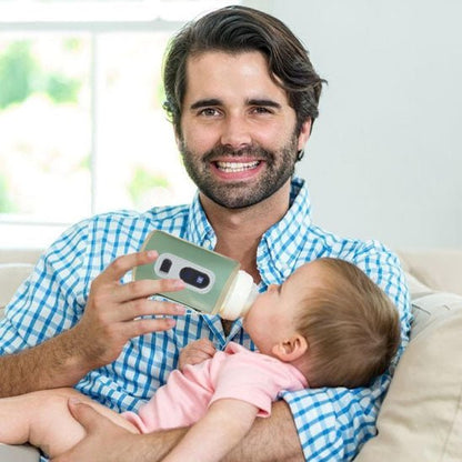 Papa utilisant un chauffe biberon nomade vert pour nourrir son bébé à la maison