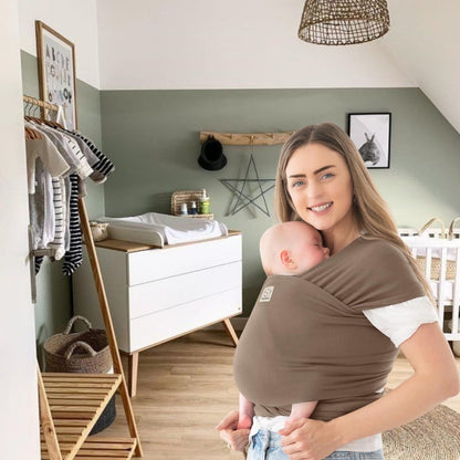 Maman portant son bébé dans une écharpe de portage bébé marron confortable à la maison, moment de tendresse et de sécurité