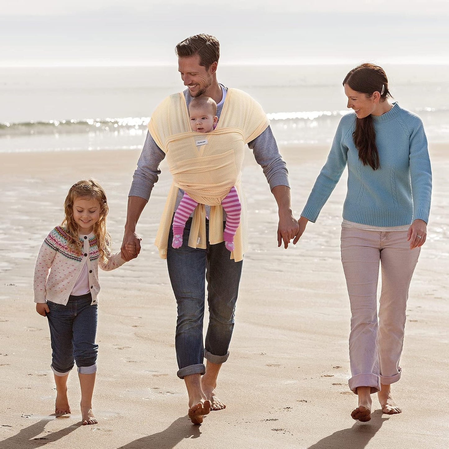 Famille se promenant sur la plage avec bébé porté en echarpe sling ergonomique