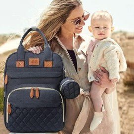 Maman moderne avec des lunettes tenant son bébé dans les bras à côté d’un sac à dos à langer