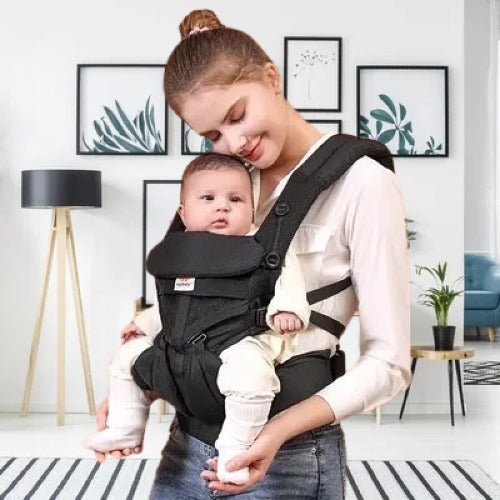 Maman portant son bébé dans un porte bebe noir ergonomique et confortable à la maison