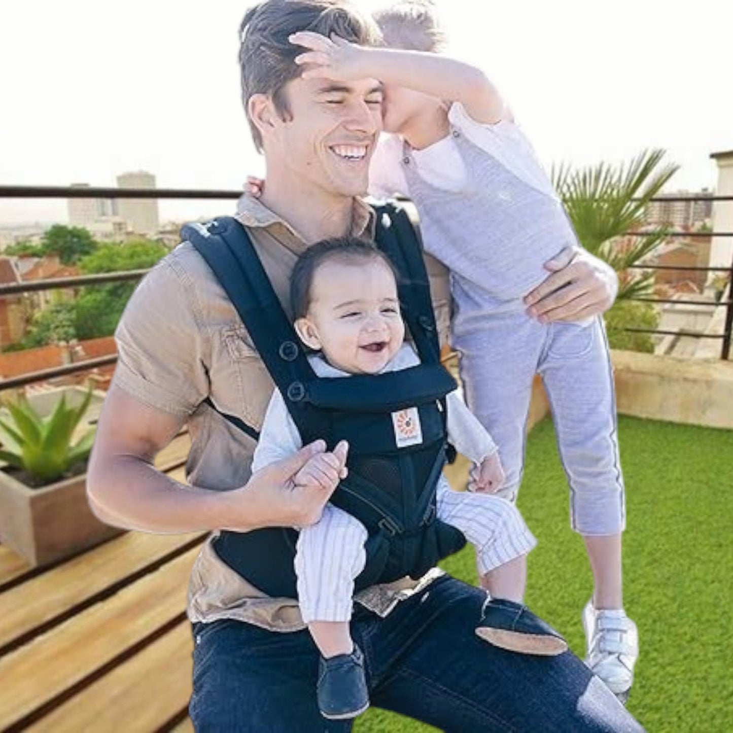 Papa portant son bébé avec porte bebe noir dans un jardin, moment de portage confortable et sécurisé