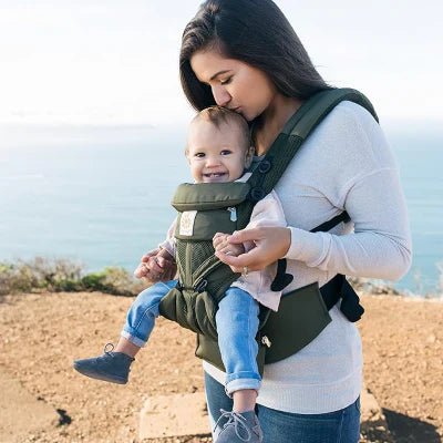 Maman portant son bébé en porte bébé pratique, profitant d’une vue sur mer