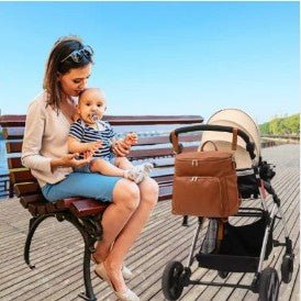 Sac à langer de luxe en cuir pu marron avec finitions dorées, porté en bandoulière et suspendu à une poussette moderne
