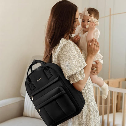 Maman portant son bébé et un sac à langer sac à dos noir pratique élégant sur le dos dans un intérieur chaleureux